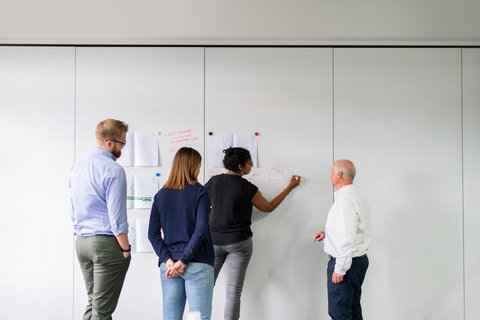 four people stand in front of a whiteboard and collect ideas