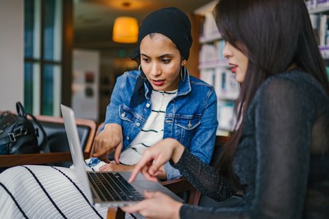 two people sitting in front of a laptop and working together